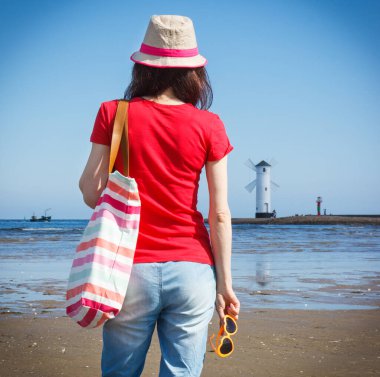 Swinoujscie 'nin batı dalgakıranı üzerinde güneş gözlüklü ve malzeme çantalı hasır şapkalı kadın, karakteristik yön bulma işareti Windmill Stawa Mlyny tarafından. Tatil ve yaz tatili