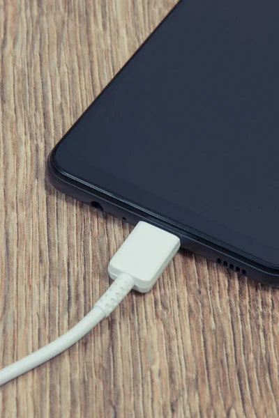 Black smartphone and connected cable of charger. Mobile phone charging