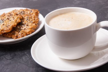 Bir fincan beyaz kahve ve taze ev yapımı yulaf ezmeli kurabiye ve farklı sağlıklı tohumlar. Lezzetli çıtır tatlı.