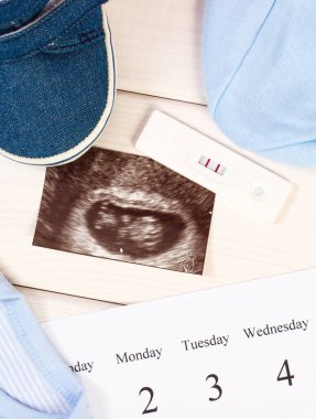 Pozitif sonuç veren hamilelik testi, bebeğin ultrason taraması, yeni doğan ve takvim için giysi, aileyi genişletme ve bebek beklemesi kavramı.