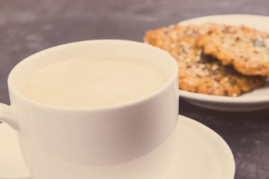 Cup of coffee with milk and fresh baked homemade oatmeal cookies with honey and different healthy seeds. Delicious crunchy dessert. Vintage photo