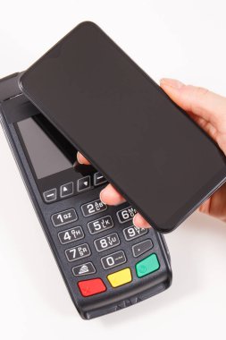 Nakitsiz ödeme yapmak için akıllı telefon ve ödeme terminalini kullanan bir kadın eli. Finans ve bankacılık kavramı