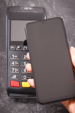 Nakitsiz ödeme yapmak için akıllı telefon ve ödeme terminalini kullanan bir kadın eli. Finans ve bankacılık kavramı