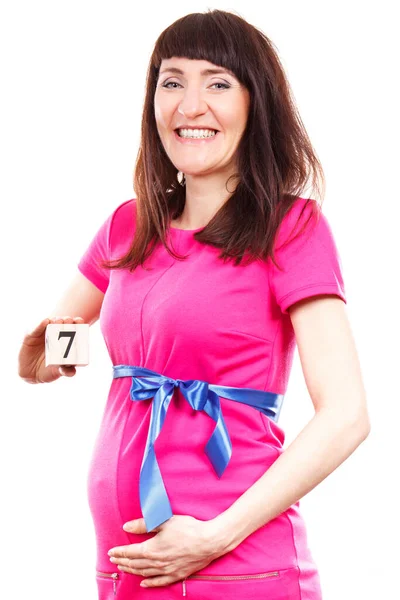 家族を拡張し 新生児のため期待しての概念の第七の月の数を示すブルーのリボンとピンクのドレスで幸せな笑顔の妊娠中の女性 — ストック写真