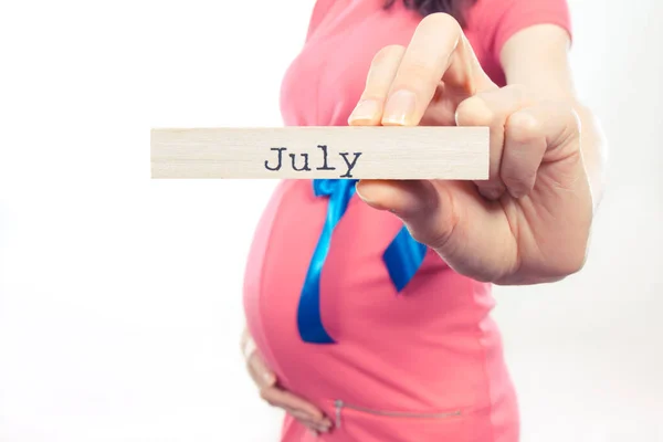 Kobieta Ciąży Ubrana Różową Sukienkę Niebieską Wstążką Napisem July Drewnianej — Zdjęcie stockowe