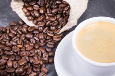 Beyaz cam bardakta kahve ve kavrulmuş kahve çekirdekleri.