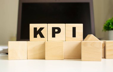 KPI kelimesi ofis masasında dizüstü bilgisayarın önünde duran tahta küplere yazılmıştır. İş konsepti.