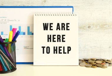 Burada yardım etmek için bulunduğumuz metnin olduğu bir defter, mali tablolarla birlikte duvara yaslanıyor. Kırtasiye ve madeni paraların yanında. İş konsepti.