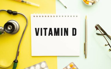 Not defterine steteskop ve sarı arka planda kalem ile VITAMIN D metni.