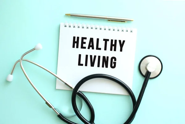 White notepad with the words HEALTHY LIVING and a stethoscope on a blue background. — Stock Photo, Image