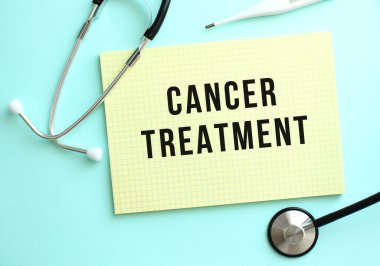 CANCER TREATMENT, mavi arkaplandaki steteskopun yanında duran sarı bir not defterine yazılmıştır. Tıbbi konsept