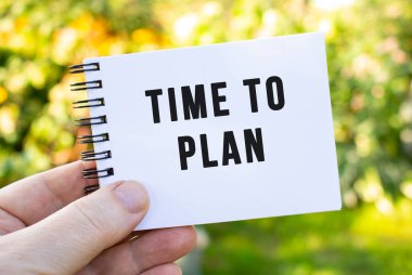 Bir adamın elinde üzerinde planlanması gereken zaman yazan bir defter var. Doğanın arka planında not defteri olan bir adam. Parktaki açık bir defterin yakın plan görüntüsü.