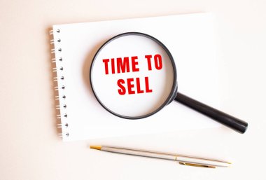 Büyüteç pedin üzerinde duruyor ve Time to sell 'i beyaz bir sayfada gösteriyor. Yanında bir dolma kalem var. İş konsepti.
