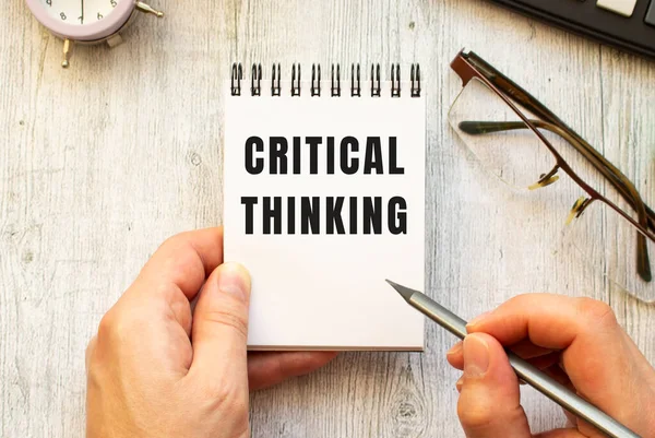 Рука пишет текст CRITICAL THINKING карандашом в блокноте. Вид сверху. Стоковое Изображение