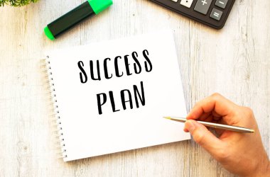 Kalemli bir el, tahta bir masanın üzerine not defterine SUCCESS PLAN yazar. Yukarıdan görüntüle.