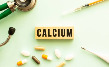 Steteskoplu ve haplı tahta bir küpte CALCIUM kelimesi. Tıbbi konsept. Düz yatıyordu.