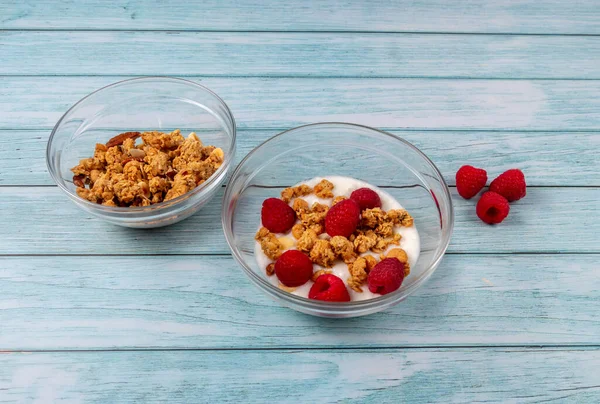 Healthy, ready-to-eat breakfast in a glass bowl, including raspberries, cereal and yogurt. Placed on a blue wooden table