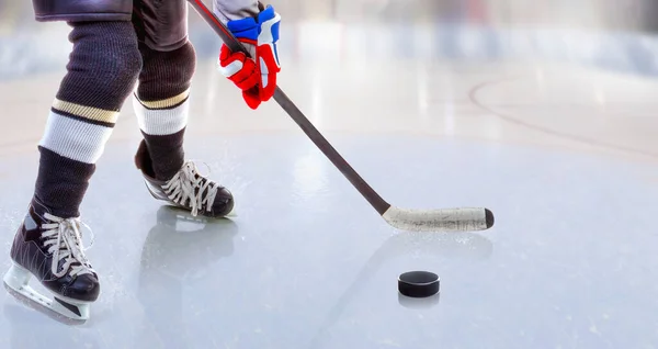 Low angle view of ice hockey player with stick on ice rink controlling puck and copy space.