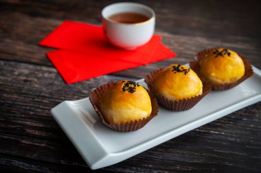 Geleneksel Çin Yeni Yıl pastaları yumuşak hamur ile pişirildi ve tuzlu yumurta sarısı ve tatlı macunla dolduruldu. Çin şanslı para paketleri kırmızı paketler ve arka plan kırsal ahşap masa üzerinde çay.