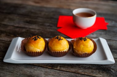 Geleneksel Çin Yeni Yıl pastaları yumuşak hamur ile pişirildi ve tuzlu yumurta sarısı ve tatlı macunla dolduruldu. Çin şanslı para paketleri kırmızı paketler ve arka plan kırsal ahşap masa üzerinde çay.