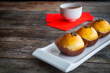 Geleneksel Çin Yeni Yıl pastaları yumuşak hamur ile pişirildi ve tuzlu yumurta sarısı ve tatlı macunla dolduruldu. Çin şanslı para paketleri kırmızı paketler ve arka plan kırsal ahşap masa üzerinde çay.