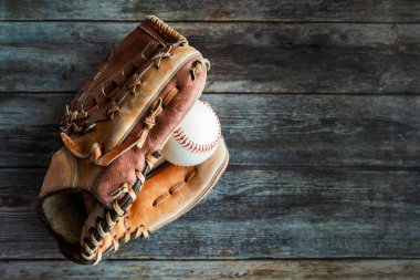Leather baseball or softball glove with ball on rustic wooden background with copy space.