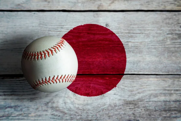 Leather baseball on rustic wooden background painted with Japanese flag with copy space. Japan is one of the top baseball nations in the world.