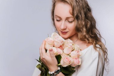 Beyaz elbiseli güzel bir kadın elinde pembe güllerle büyük bir buket tutuyor..