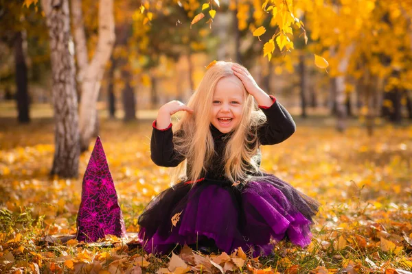 Маленькая Милая Блондинка Костюме Ведьмы Бросает Листья Парке Осенью Улыбается — стоковое фото