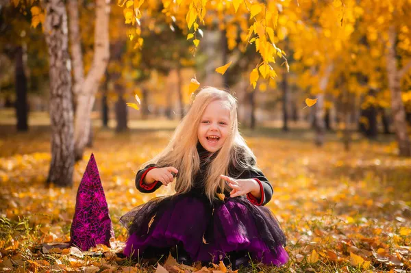 Маленькая Милая Блондинка Костюме Ведьмы Бросает Листья Парке Осенью Улыбается — стоковое фото