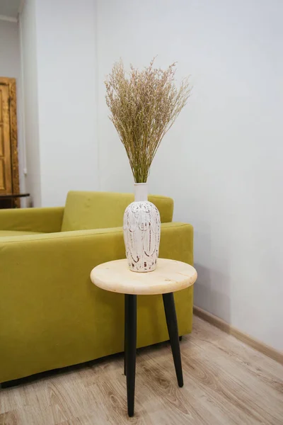 白い花瓶のドライな野の花の花束は 緑のソファの背景にコーヒーテーブルの上に立っています 内装の装飾植物 — ストック写真