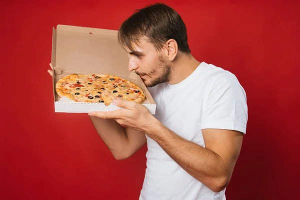 Мужчина Улыбкой Белой Футболке Красном Фоне Держит Коробку Аппетитной Пиццей — стоковое фото