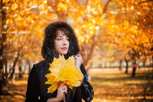 秋の森の中に長い黒い髪の女性が手にカエデの葉の花束を持っています 9月と10月の森の中を歩く — ストック写真