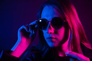 Geceleri parlayan pembe neon şehrin yakınında uzun saçlı tatlı bir kız. Genç bir kadının boyalı mavi pembe saçları. Yuvarlak gözlüklü gizemli yeniyetme. Siber punk ışık yansıması.