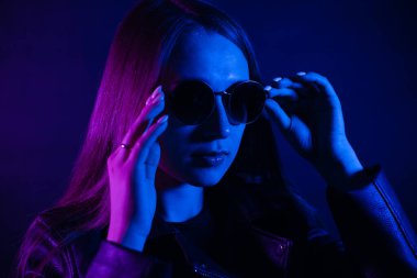 Geceleri parlayan pembe neon şehrin yakınında uzun saçlı tatlı bir kız. Genç bir kadının boyalı mavi pembe saçları. Yuvarlak gözlüklü gizemli yeniyetme. Siber punk ışık yansıması.