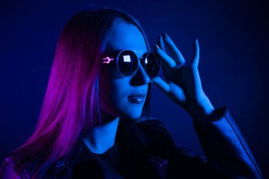 Geceleri parlayan pembe neon şehrin yakınında uzun saçlı tatlı bir kız. Genç bir kadının boyalı mavi pembe saçları. Yuvarlak gözlüklü gizemli yeniyetme. Siber punk ışık yansıması.