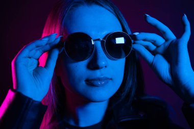 Geceleri parlayan pembe neon şehrin yakınında uzun saçlı tatlı bir kız. Genç bir kadının boyalı mavi pembe saçları. Yuvarlak gözlüklü gizemli yeniyetme. Siber punk ışık yansıması.