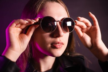 Geceleri parlayan pembe neon şehrin yakınında uzun saçlı tatlı bir kız. Genç bir kadının boyalı mavi pembe saçları. Yuvarlak gözlüklü gizemli yeniyetme. Siber punk ışık yansıması.