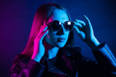 Geceleri parlayan pembe neon şehrin yakınında uzun saçlı tatlı bir kız. Genç bir kadının boyalı mavi pembe saçları. Yuvarlak gözlüklü gizemli yeniyetme. Siber punk ışık yansıması.
