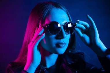 Geceleri parlayan pembe neon şehrin yakınında uzun saçlı tatlı bir kız. Genç bir kadının boyalı mavi pembe saçları. Yuvarlak gözlüklü gizemli yeniyetme. Siber punk ışık yansıması.