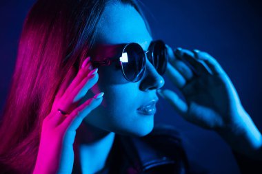 Geceleri parlayan pembe neon şehrin yakınında uzun saçlı tatlı bir kız. Genç bir kadının boyalı mavi pembe saçları. Yuvarlak gözlüklü gizemli yeniyetme. Siber punk ışık yansıması.