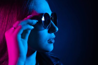 Geceleri parlayan pembe neon şehrin yakınında uzun saçlı tatlı bir kız. Genç bir kadının boyalı mavi pembe saçları. Yuvarlak gözlüklü gizemli yeniyetme. Siber punk ışık yansıması.