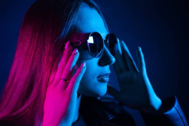 Geceleri parlayan pembe neon şehrin yakınında uzun saçlı tatlı bir kız. Genç bir kadının boyalı mavi pembe saçları. Yuvarlak gözlüklü gizemli yeniyetme. Siber punk ışık yansıması.