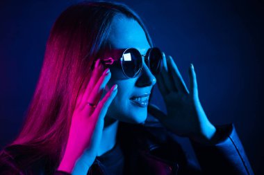 Geceleri parlayan pembe neon şehrin yakınında uzun saçlı tatlı bir kız. Genç bir kadının boyalı mavi pembe saçları. Yuvarlak gözlüklü gizemli yeniyetme. Siber punk ışık yansıması.