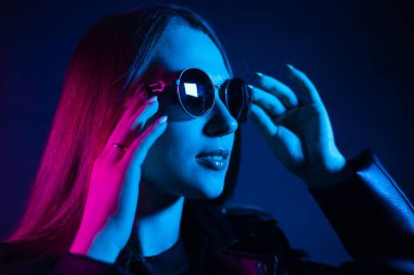 Geceleri parlayan pembe neon şehrin yakınında uzun saçlı tatlı bir kız. Genç bir kadının boyalı mavi pembe saçları. Yuvarlak gözlüklü gizemli yeniyetme. Siber punk ışık yansıması.