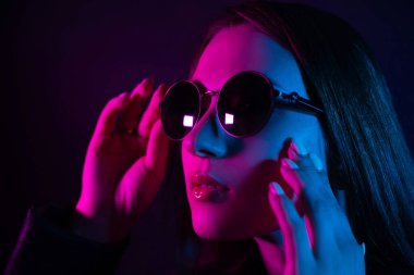 Geceleri parlayan pembe neon şehrin yakınında uzun saçlı tatlı bir kız. Genç bir kadının boyalı mavi pembe saçları. Yuvarlak gözlüklü gizemli yeniyetme. Siber punk ışık yansıması.