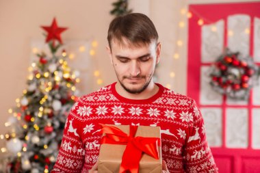 Noel ağacının önünde İskandinav desenli süveter giyen genç bir adam..