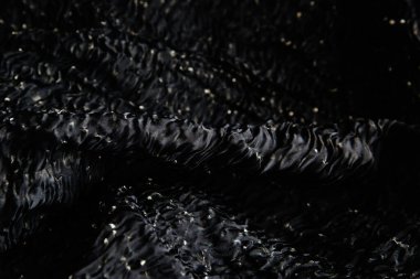 Buruşmuş siyah kumaş kıvrımlar ve kumaşların içinde yatıyor. Koyu renkli tekstil dokusu
