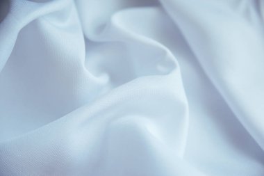 Buruşmuş beyaz kumaş kıvrımlar ve kumaşların içinde yatıyor. Beyaz tekstil dokusu