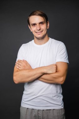 Beyaz tişörtlü yakışıklı genç bir adam gri bir arka planda duruyor. Yazıt için giysiler. maketleme